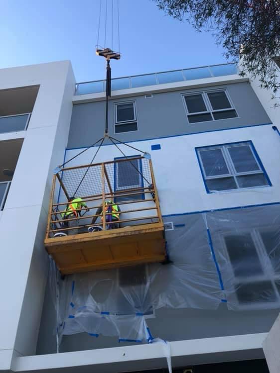 Professional painters using a crane-operated work platform for safe high-access exterior painting on a commercial building