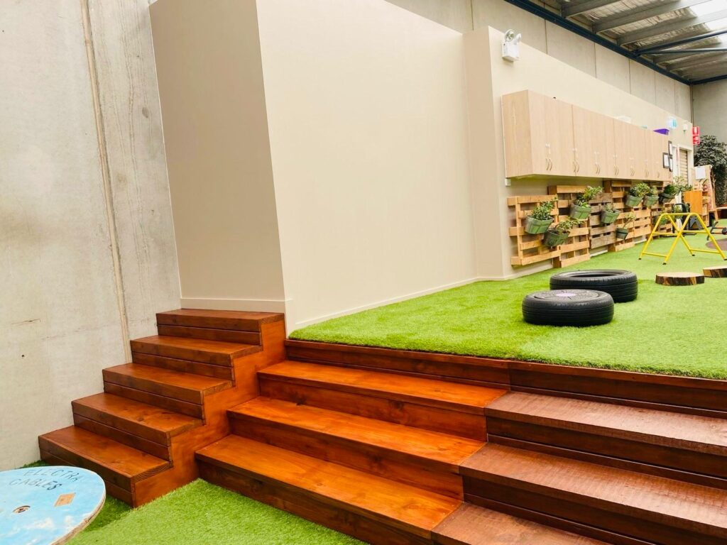 Polished wood stain finish on tiered indoor timber steps leading to an artificial grass play surface