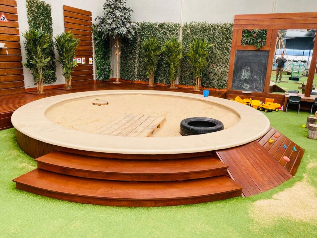 High-gloss varnish finish on custom timber circular seating and a wooden sandpit border